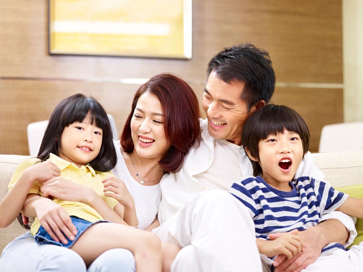 portrait of a happy asian family sitting on couch at home, smiling and laughing.